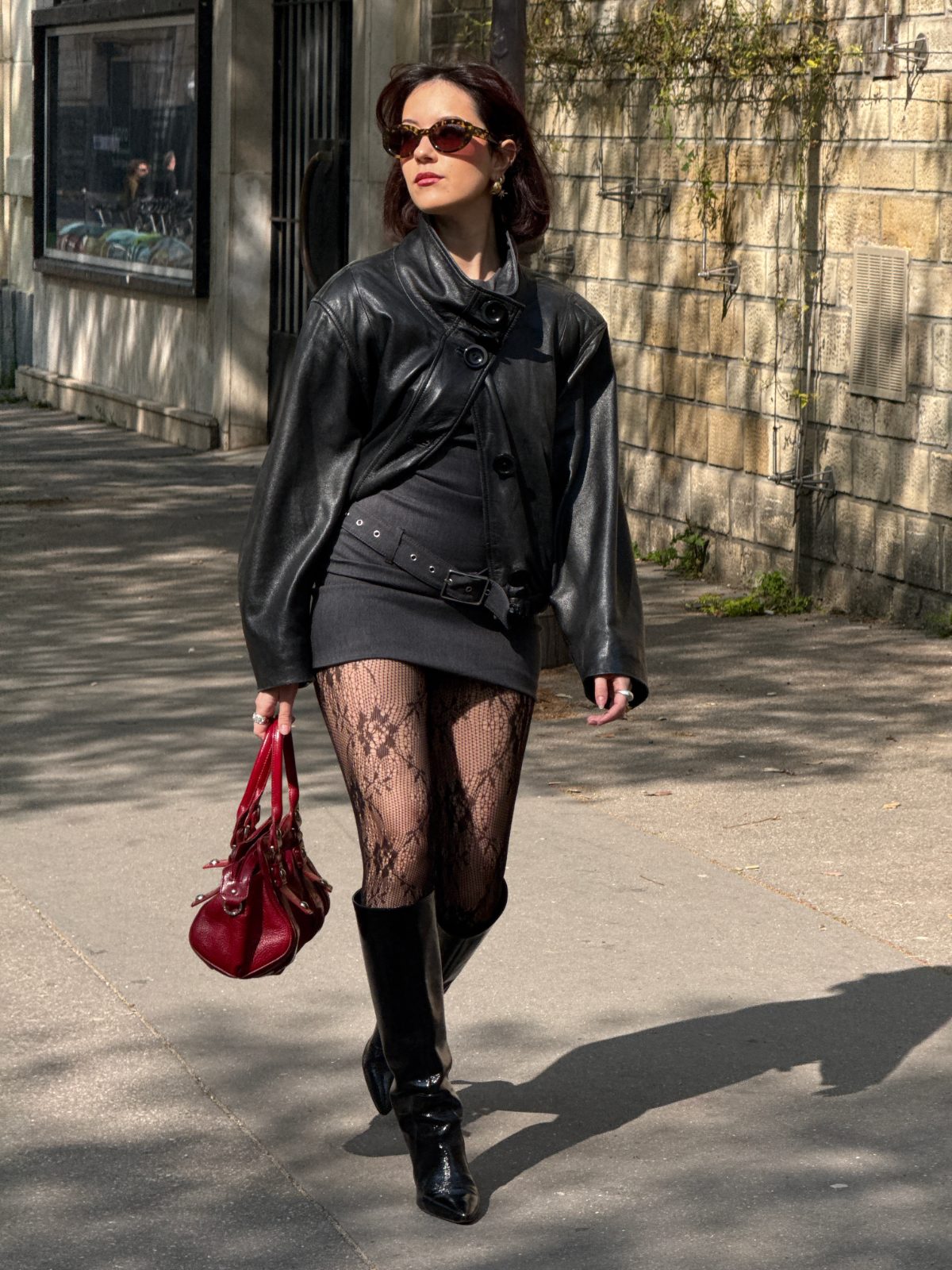 Black leather jacket, charcoal mini dress, patterned tights, knee-high boots, and red handbag.