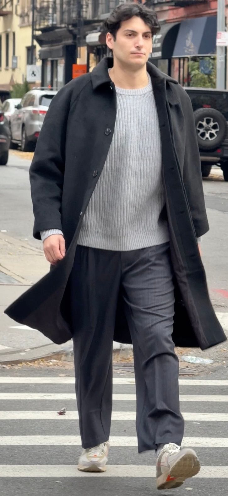 Black trench coat, gray ribbed sweater, pinstripe trousers, and neutral sneakers on street.