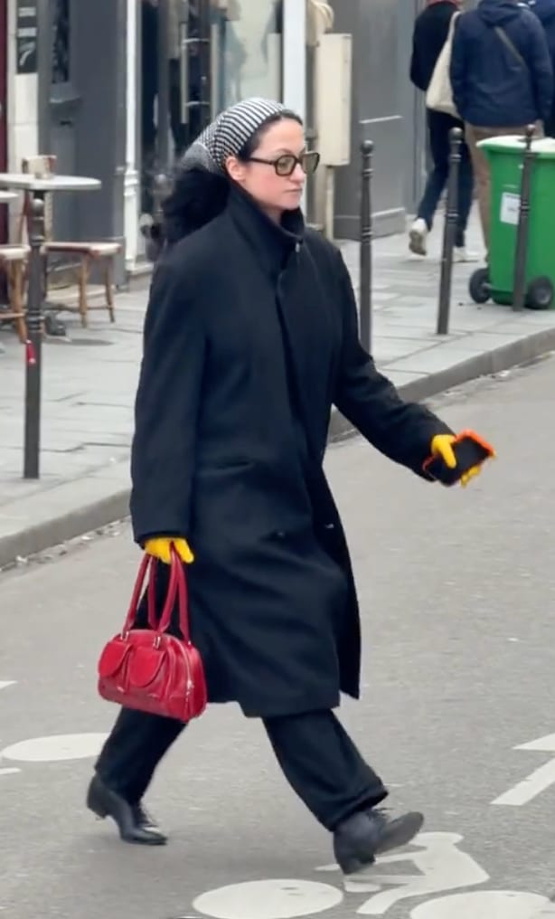 Black coat, striped headscarf, yellow gloves, and red handbag on a street.