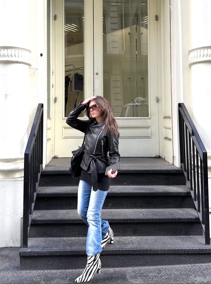 Black leather belted jacket, light wash jeans, and zebra print boots descending stairs.