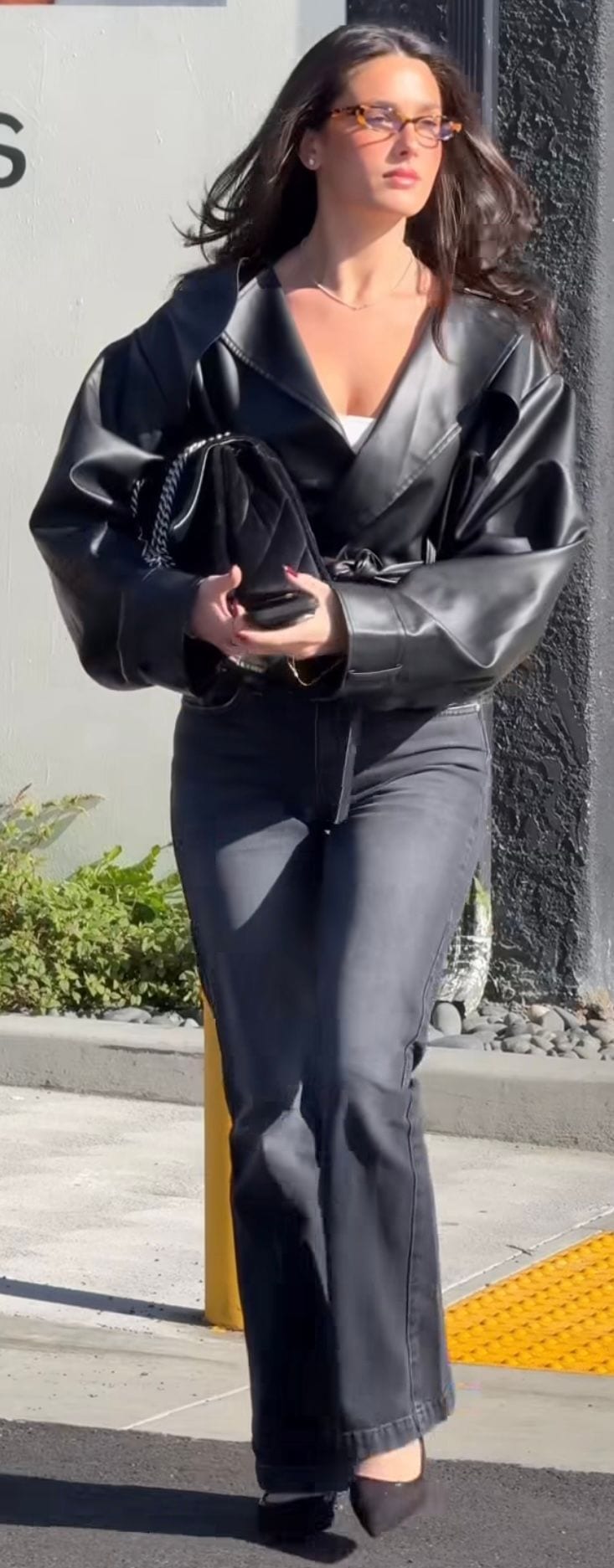 Black oversized leather jacket, white top, grey jeans, and a quilted black handbag.