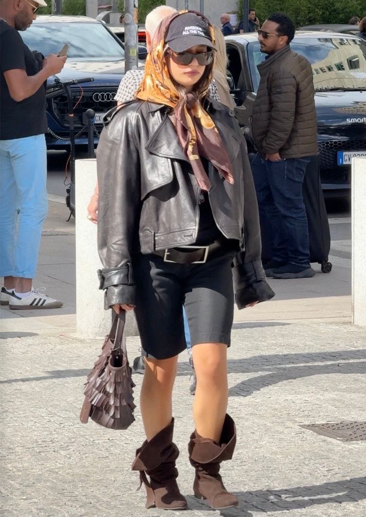Black leather jacket, biker shorts, brown slouch boots, patterned silk scarf, black baseball cap.