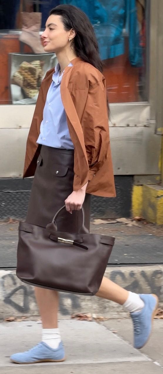 Brown jacket over light blue shirt, dark brown midi skirt, brown tote bag, light blue sneakers.