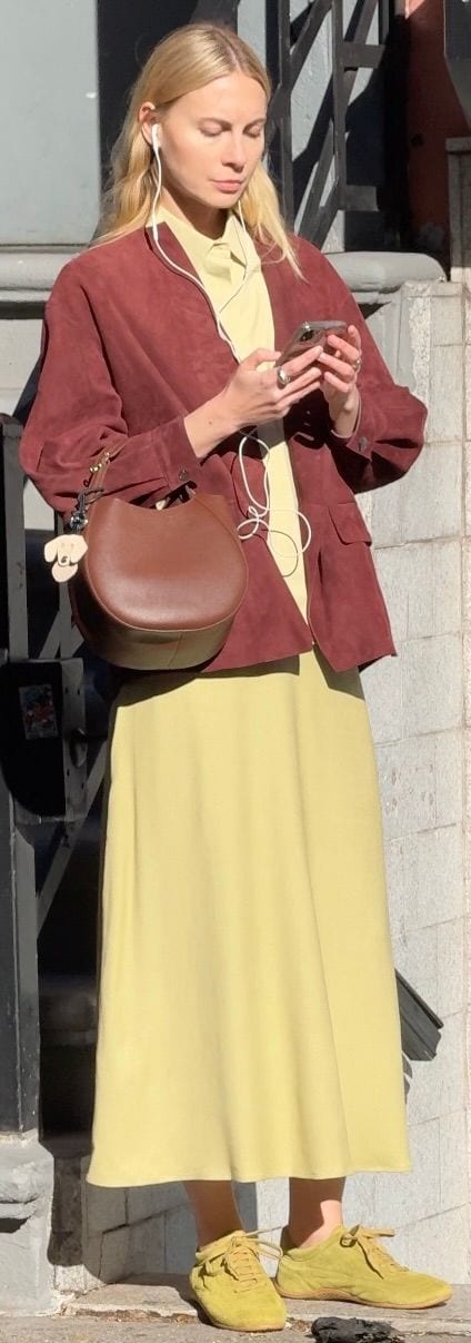 Suede burgundy jacket over a lime shirt and midi skirt, with yellow sneakers and a brown bag.
