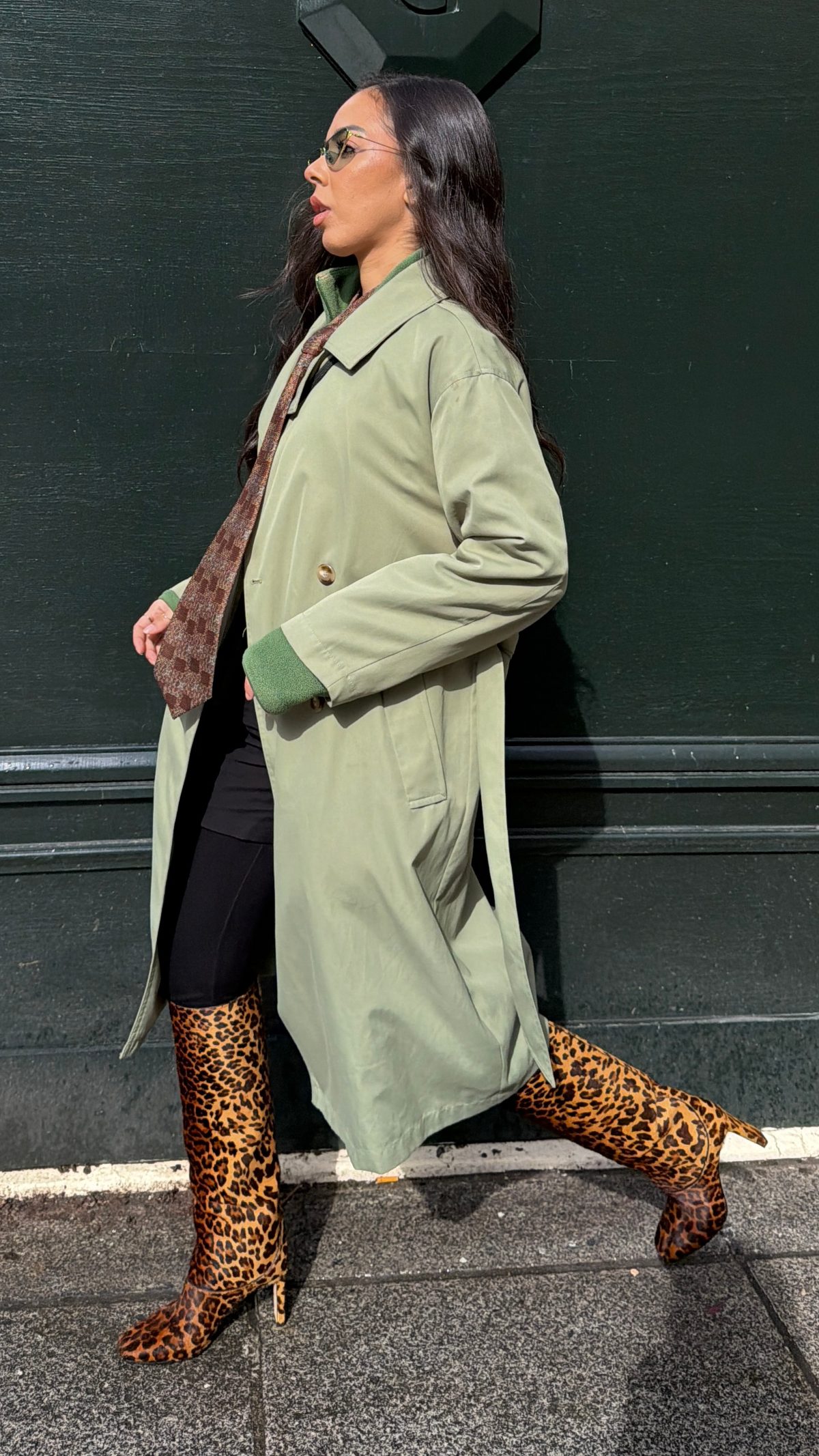 Olive green trench coat, black pants, green sweater cuffs, brown checkered tie, and leopard print boots.