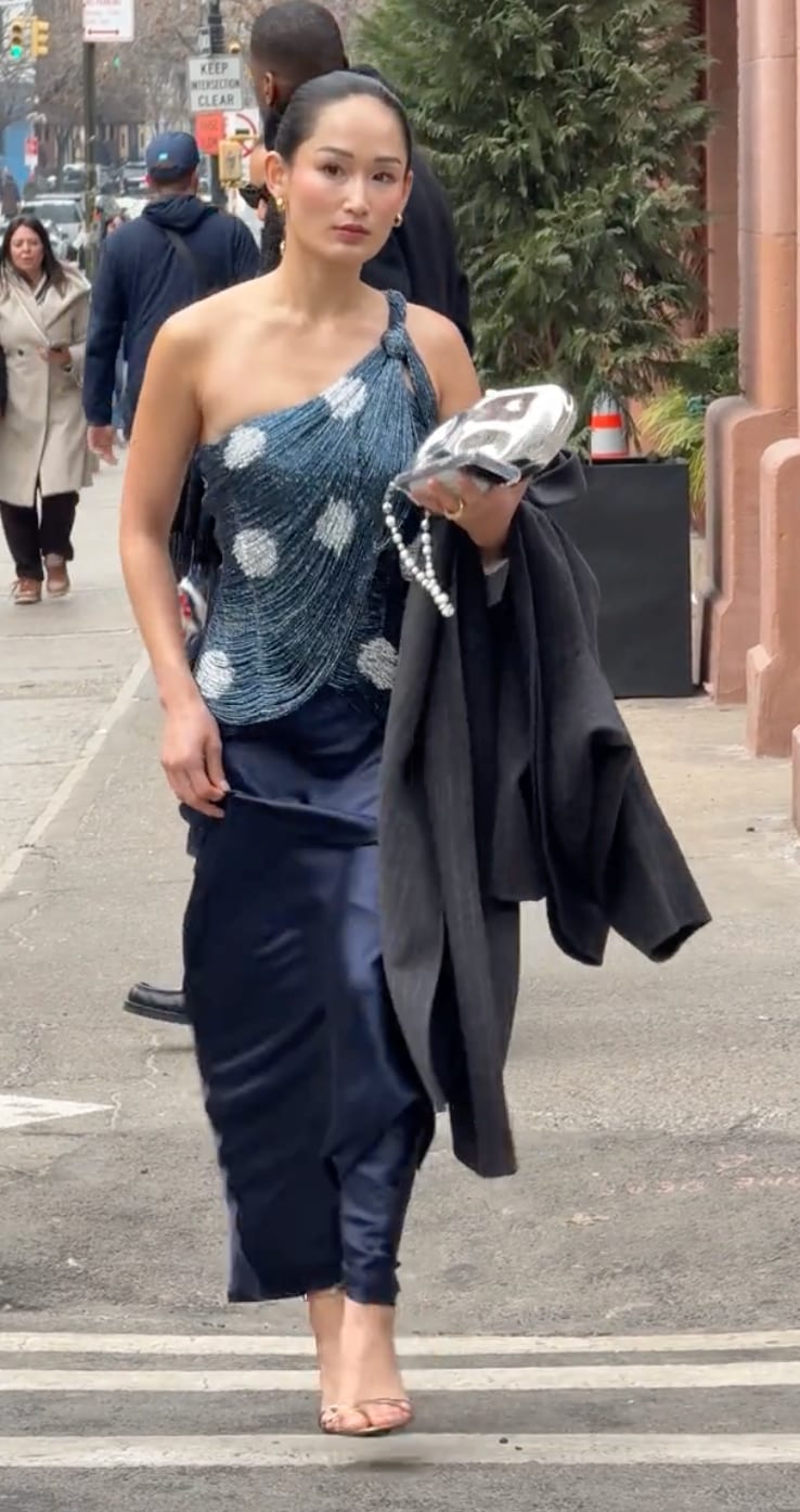 Blue beaded one-shoulder top with white polka dots, navy skirt, and beige heels.