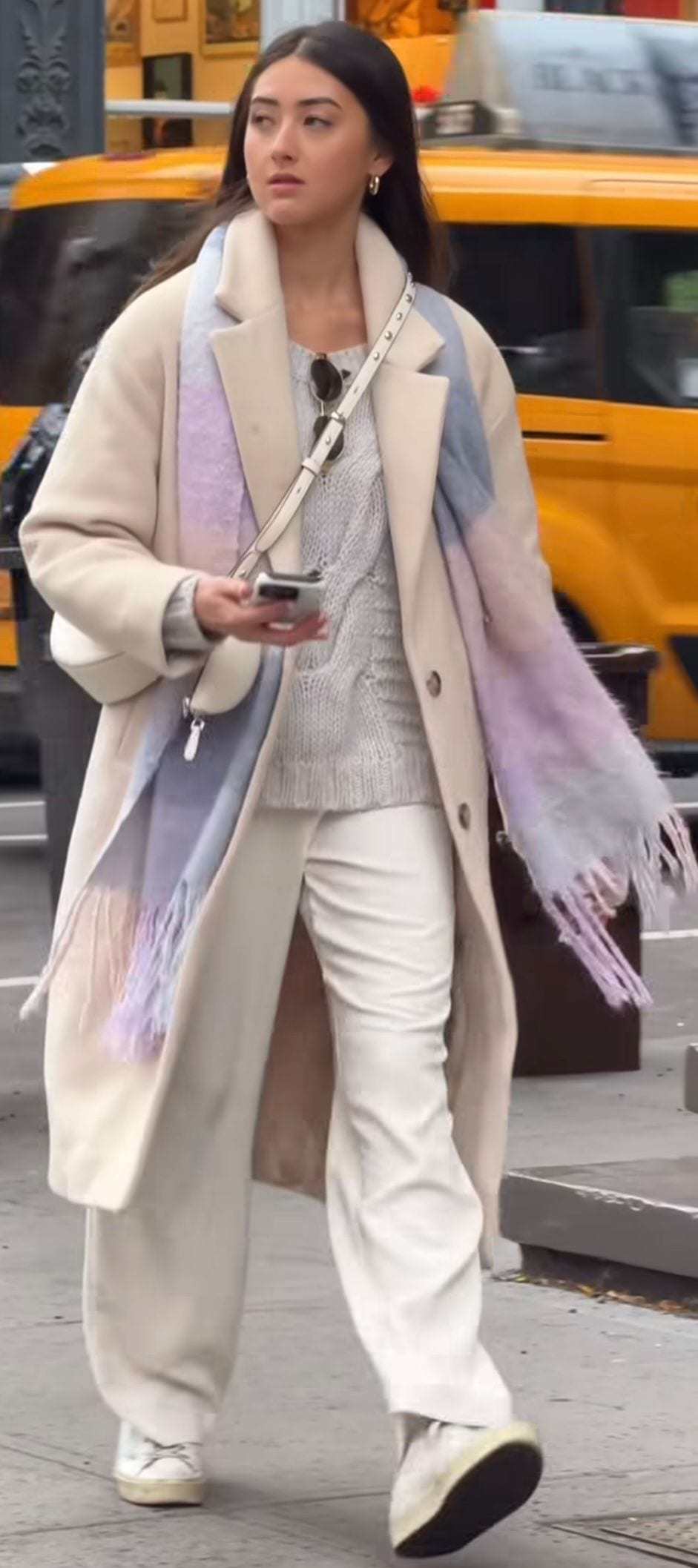 Cream trench coat, grey cable-knit sweater, white pants, multicolored scarf, and white sneakers.