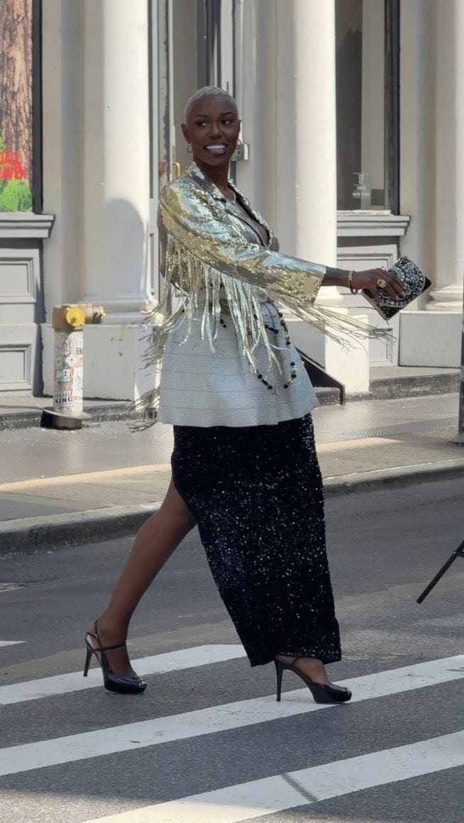 Gold sequined fringe jacket over white top and black sequin skirt, black heels, and clutch.