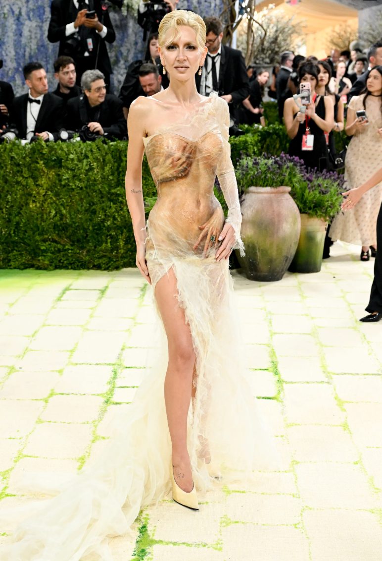 Sheer, distressed beige gown with body contouring, single long sleeve, and dramatic train.