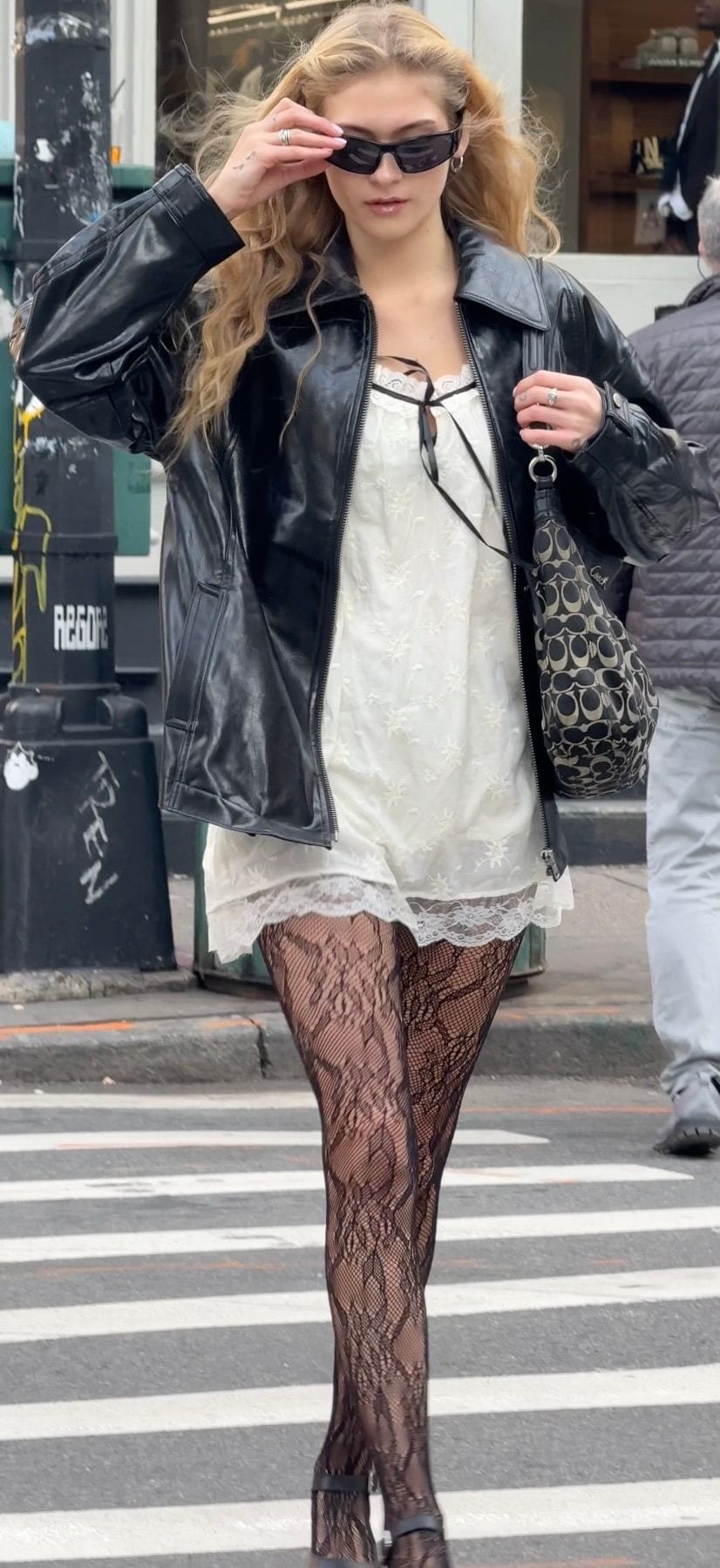 Black leather jacket, white lace mini dress, patterned tights, black sunglasses, Coach bag.