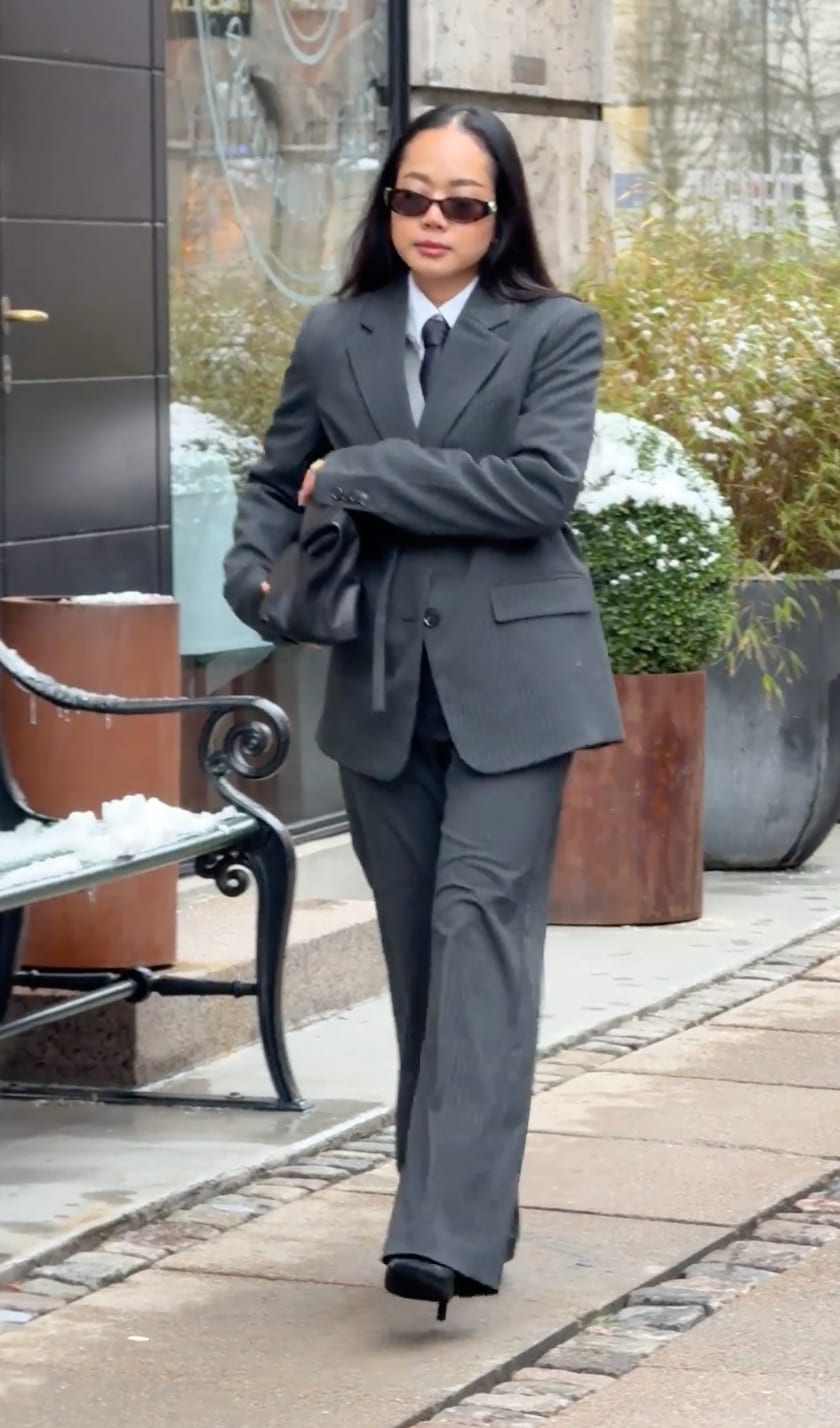 Gray pinstripe suit with white shirt, black tie, cat-eye sunglasses, and handbag.