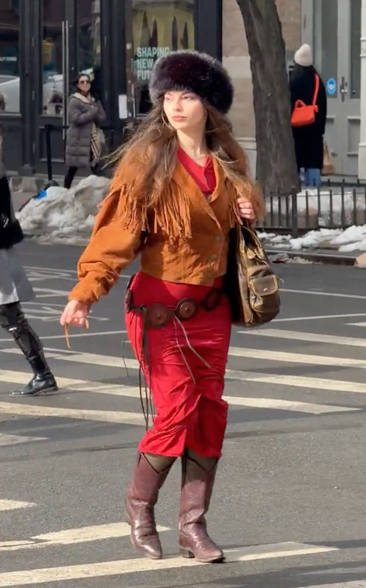 Red ruched dress, fringed suede jacket, fur hat, and cowboy boots on a city street.