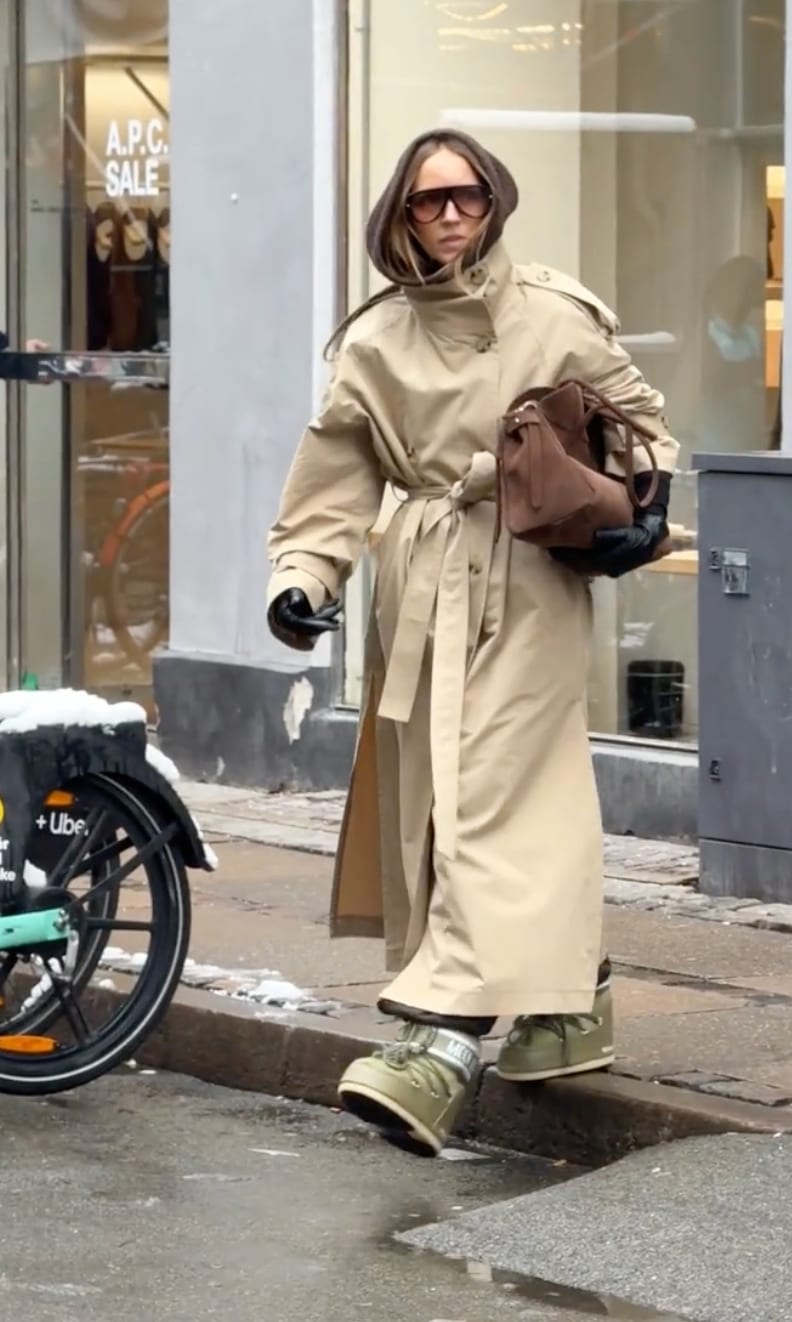 Tan trench coat with hood, brown bag, black gloves, and olive green moon boots.