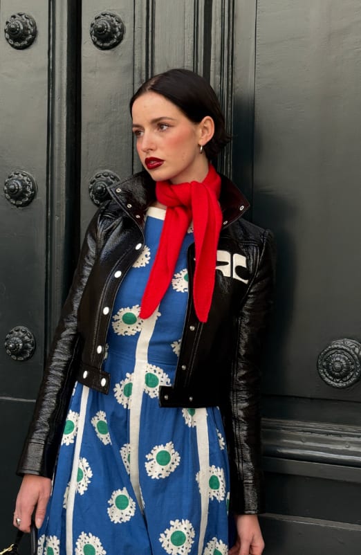 Black patent leather jacket, blue floral dress, and red scarf against a dark door.
