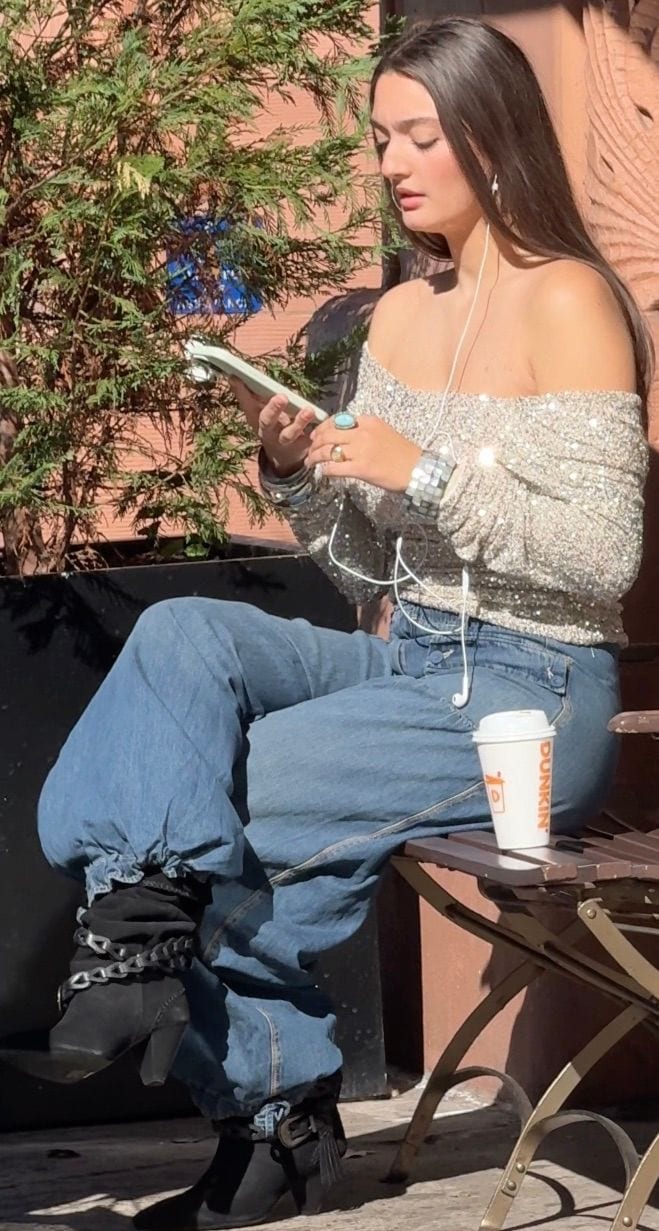 Off-shoulder sequin top, baggy jeans, black ankle boots with chain and fringe details.