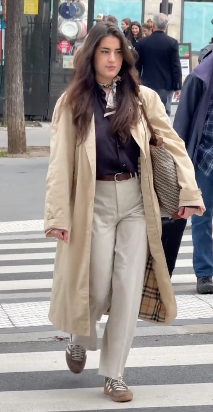 Beige trench coat with plaid lining, black shirt, light trousers, brown sneakers, and patterned scarf.