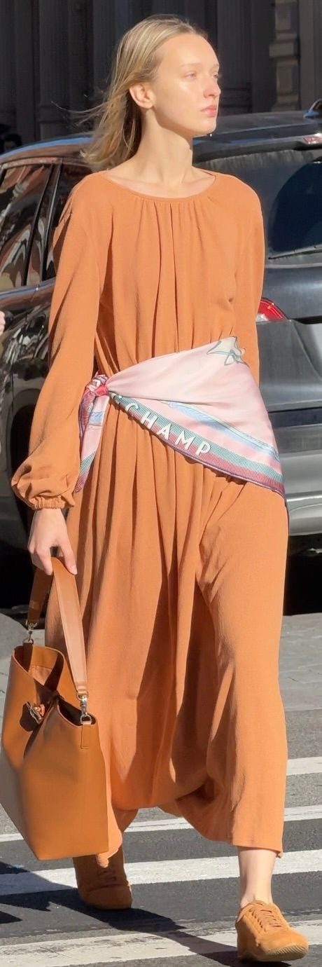 Terracotta wide-leg jumpsuit, pastel scarf belt, and brown leather bucket bag.
