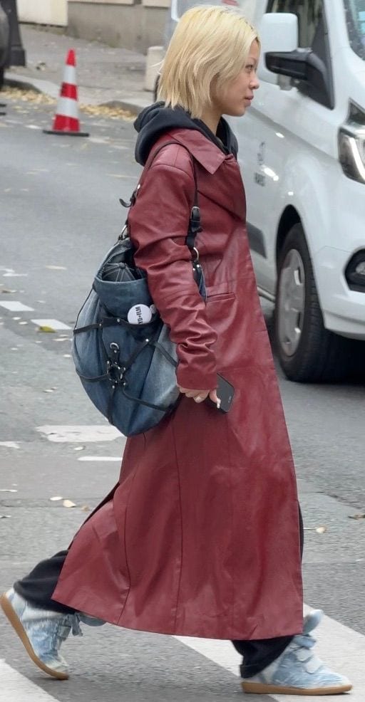 Red leather trench coat with black hoodie, denim bag, and light blue sneakers.
