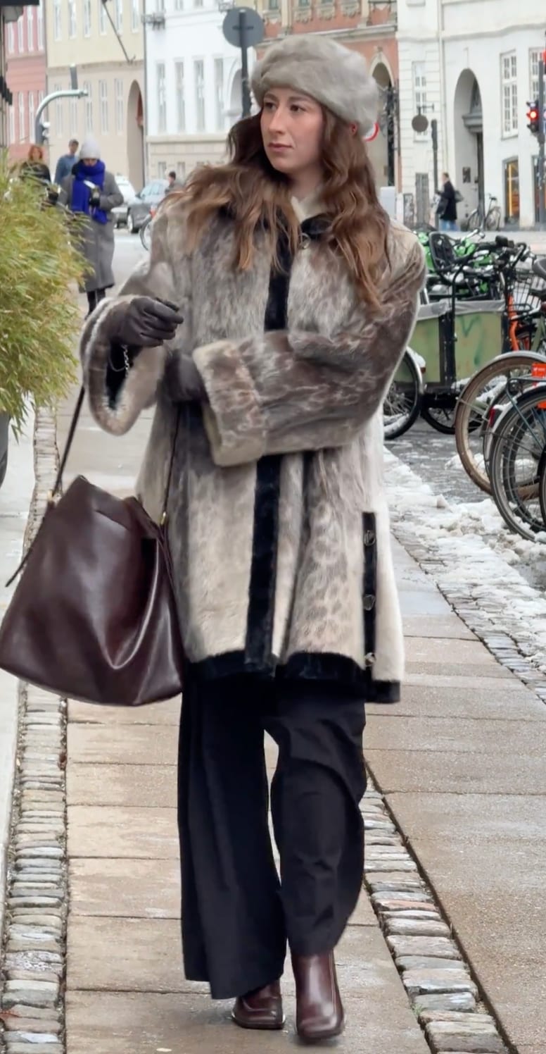 Brown fur coat with black trim, matching beret, dark trousers, and brown boots on a snowy street.