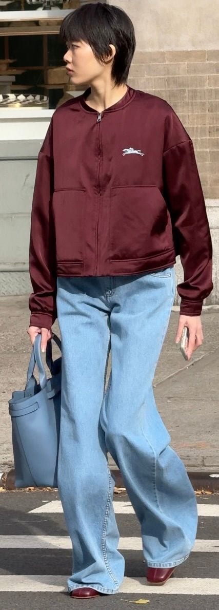 Burgundy bomber jacket, light blue wide-leg jeans, matching blue tote bag, and red flats.