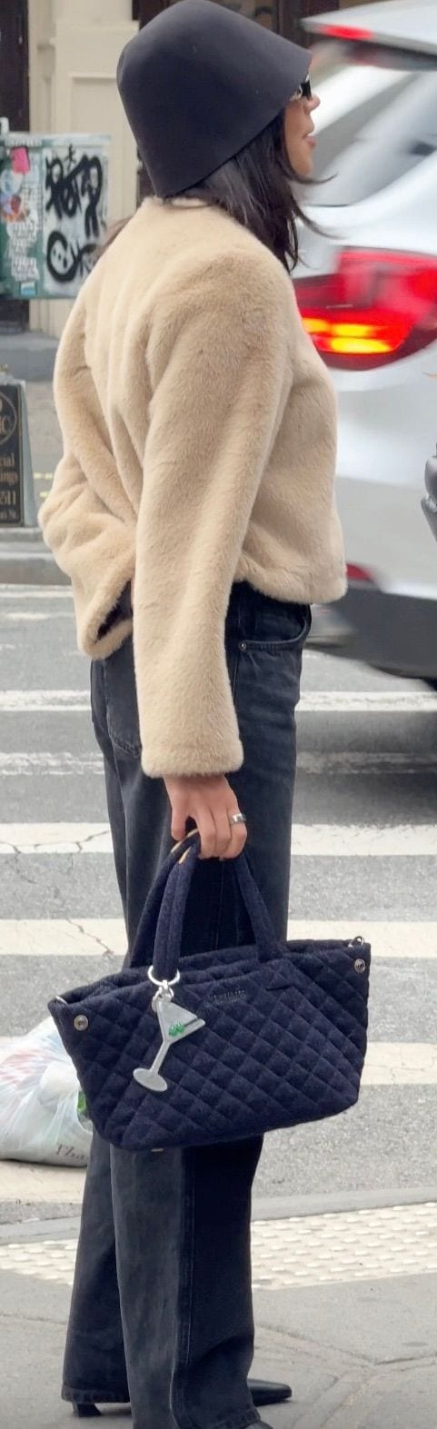 Black bucket hat, beige faux fur jacket, dark wash jeans, quilted navy handbag.