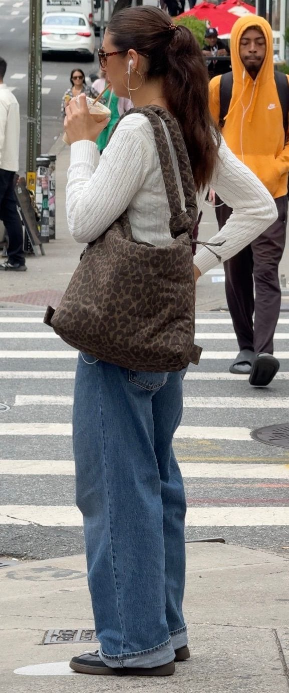 White cable-knit sweater, baggy jeans, brown leopard print bag, and sunglasses on a street.
