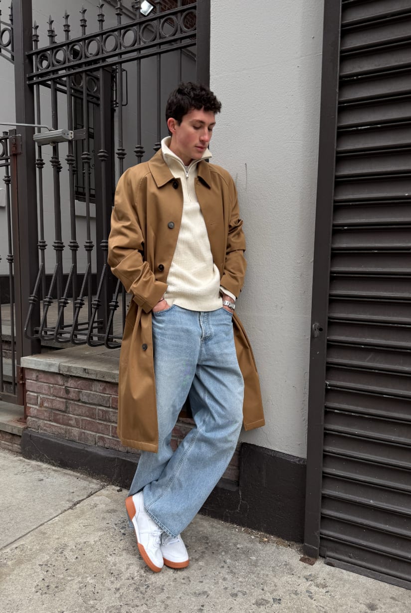 Brown trench coat over an ecru ribbed quarter-zip, light wash wide-leg jeans, white sneakers.