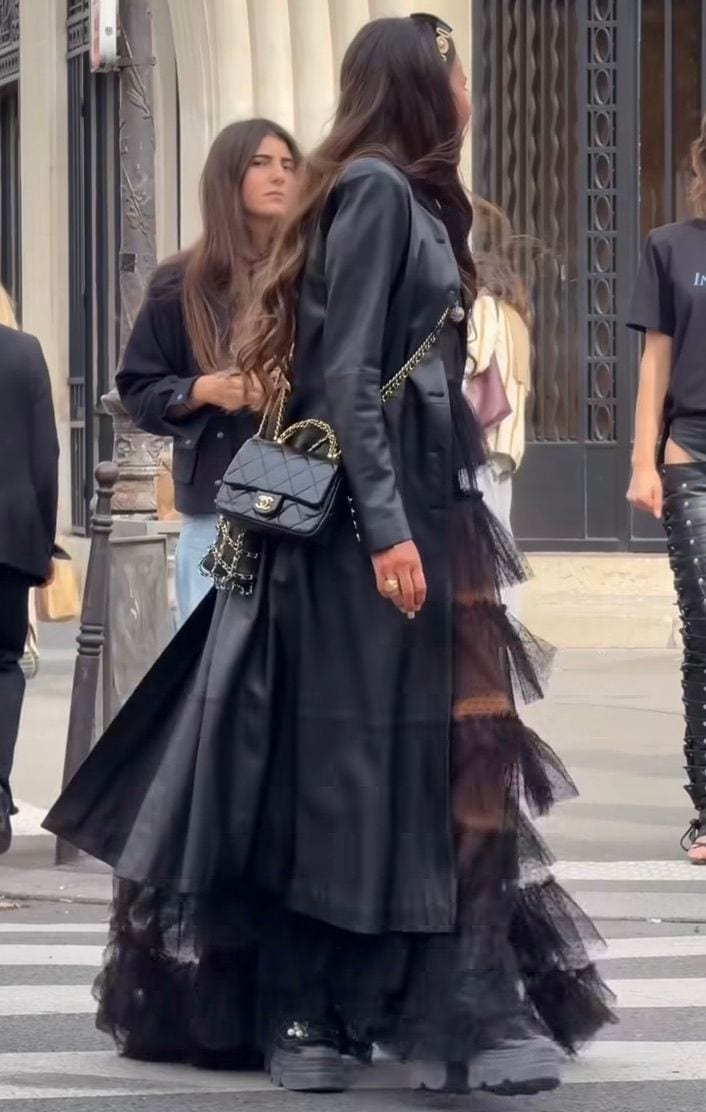 Black satin coat over a voluminous tiered tulle maxi skirt, quilted Chanel bag.
