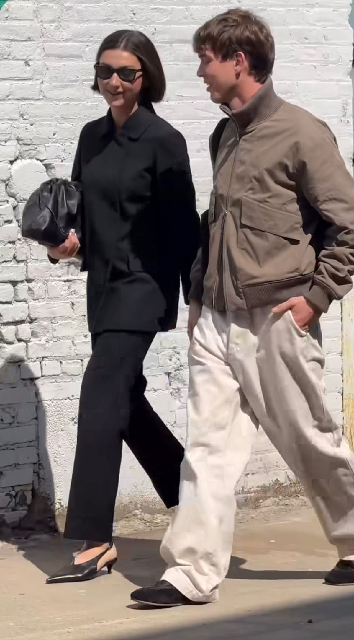 Black collared shirt with wide-leg pants, paired with a brown bomber jacket and white pants.