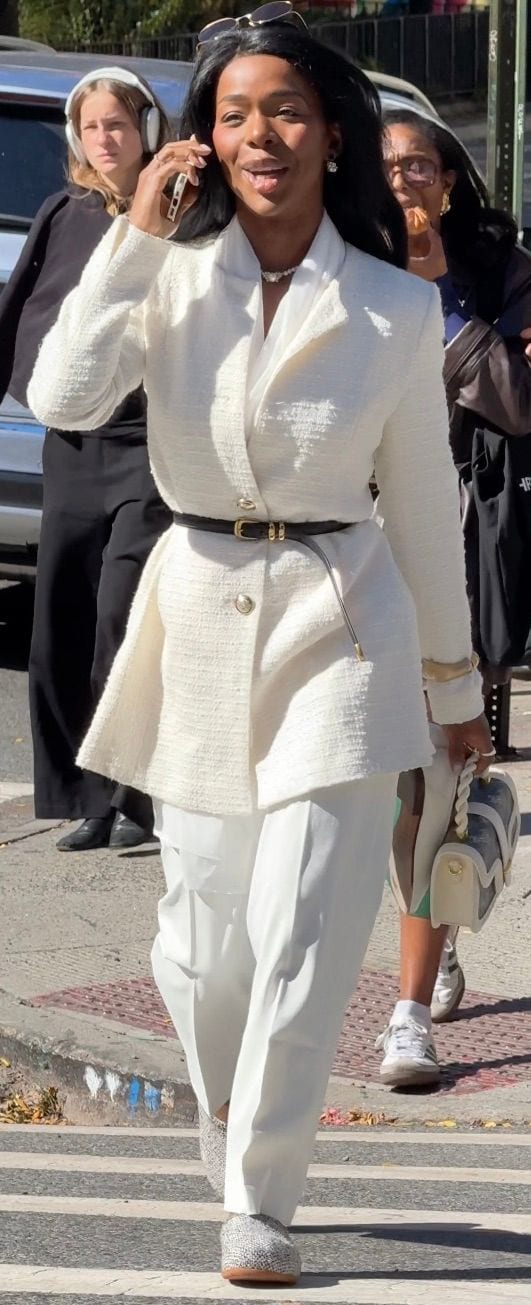 White textured blazer and trousers, black belt, sparkling shoes, and white handbag.