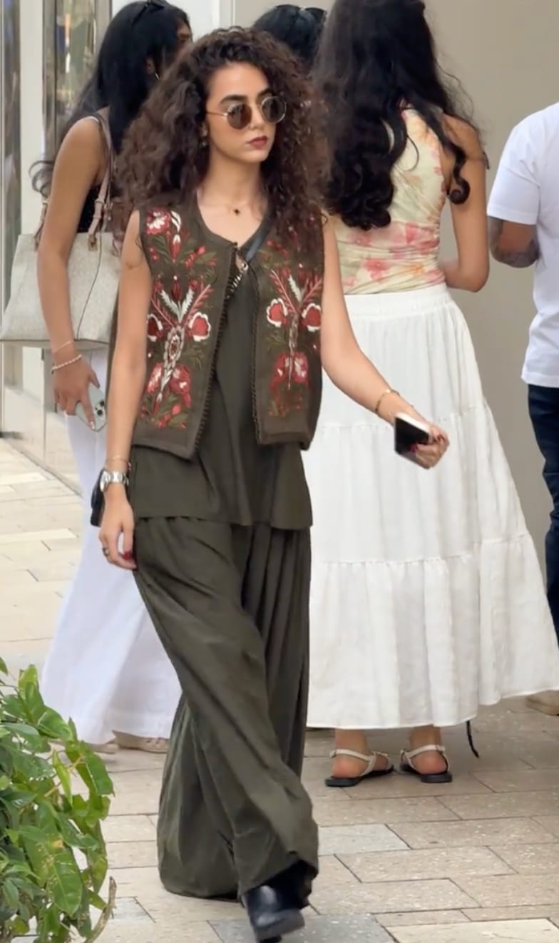 Olive green tunic and wide-leg pants with an embroidered vest and round sunglasses.