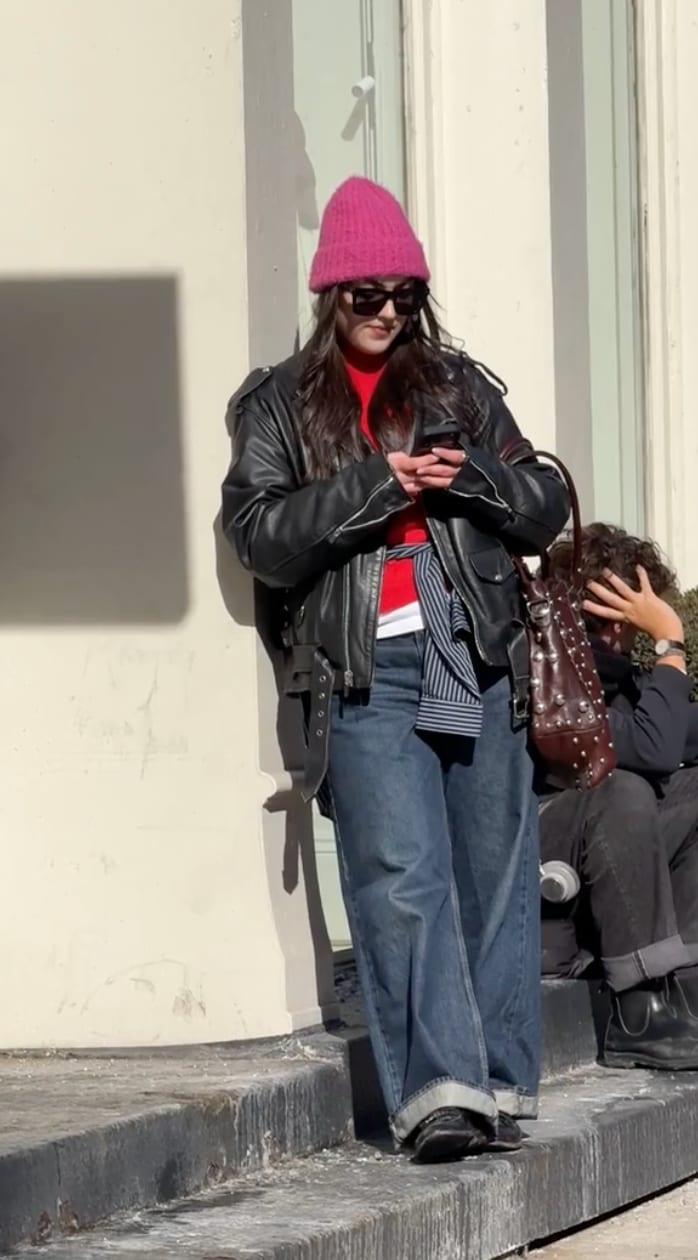 Pink knit beanie, black leather jacket, red top, baggy jeans, and studded brown bag.