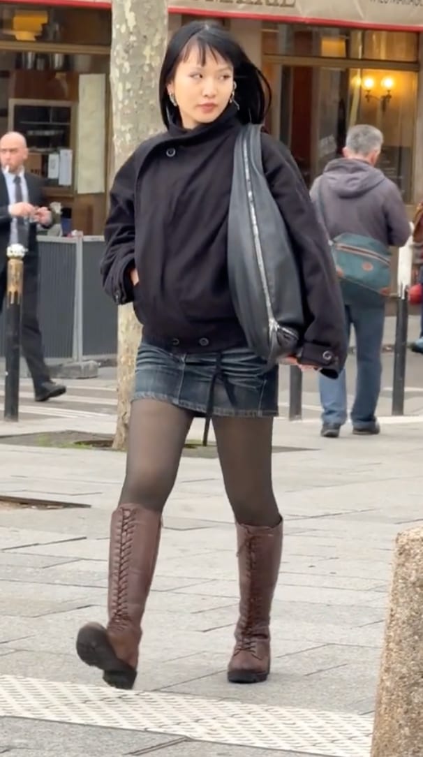 Black collared jacket, denim mini skirt, dark tights, and brown lace-up boots.