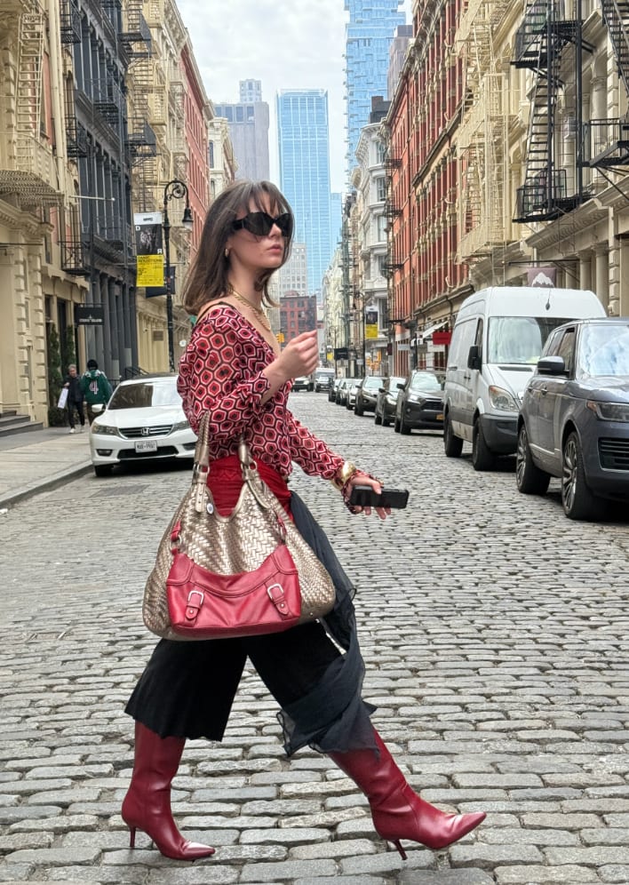 Red patterned blouse, black culottes, and red heeled boots on a cobblestone street.